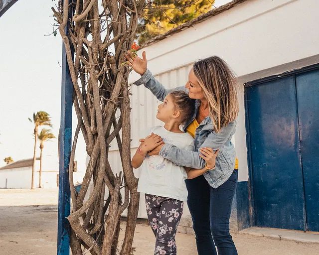 Una mujer y una niña están de pie junto a un árbol.