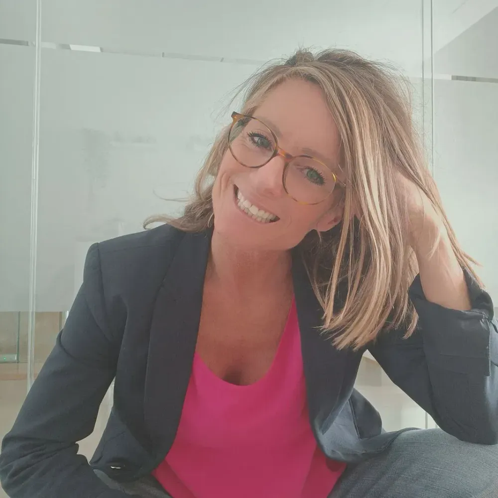 Una mujer que lleva gafas y una camisa rosa sonríe para la cámara.