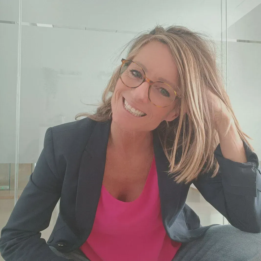 Una mujer que lleva gafas y una camisa rosa sonríe para la cámara.