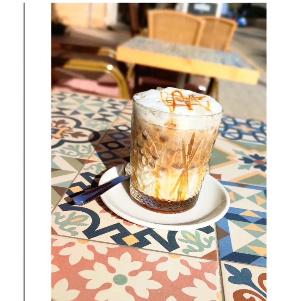 Café helado con gotas de caramelo sobre una mesa estampada en un café soleado al aire libre.