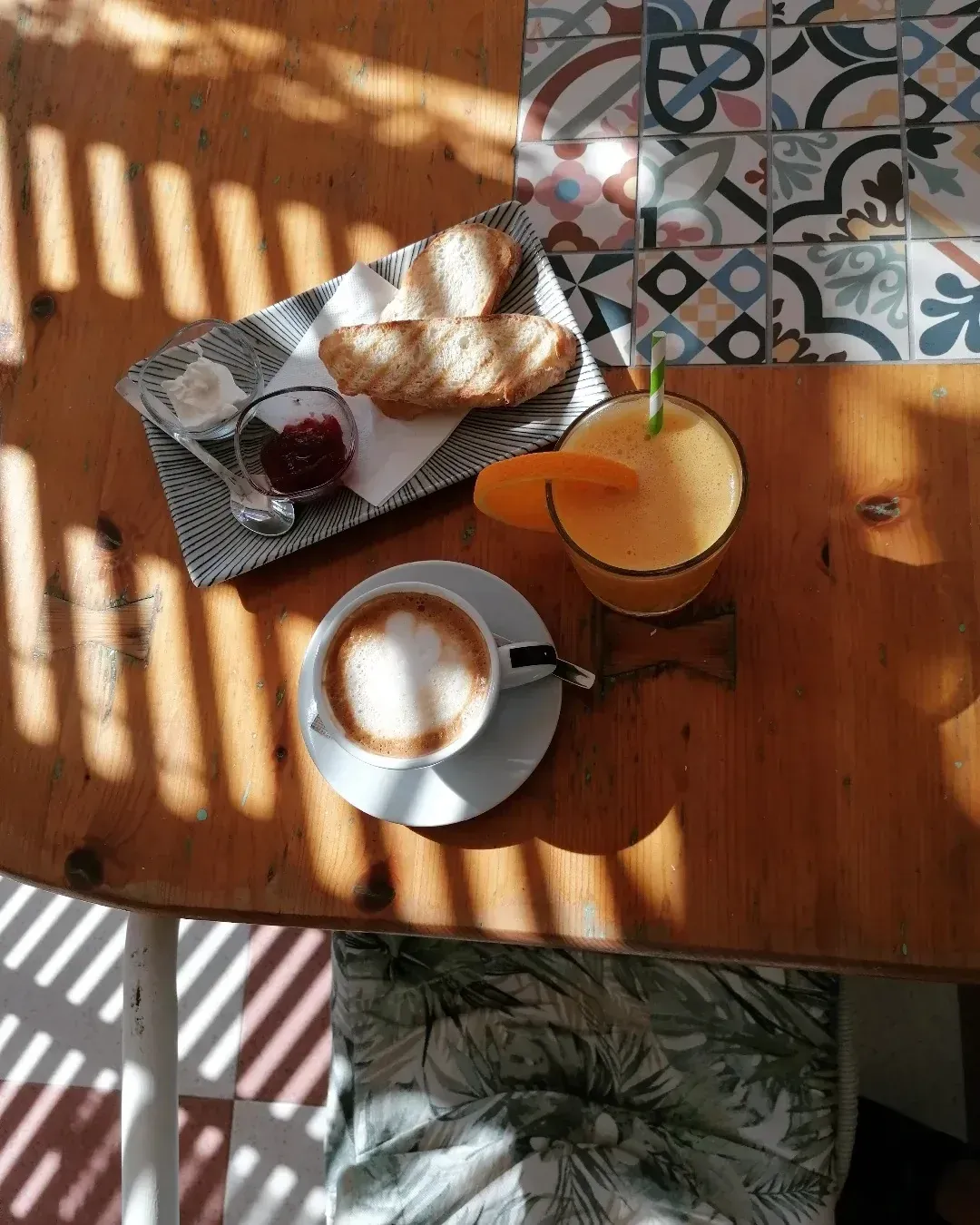 Desayuno en una mesa de madera: café, jugo con rodaja de naranja, pastel con mermelada, sombras de la luz del sol.