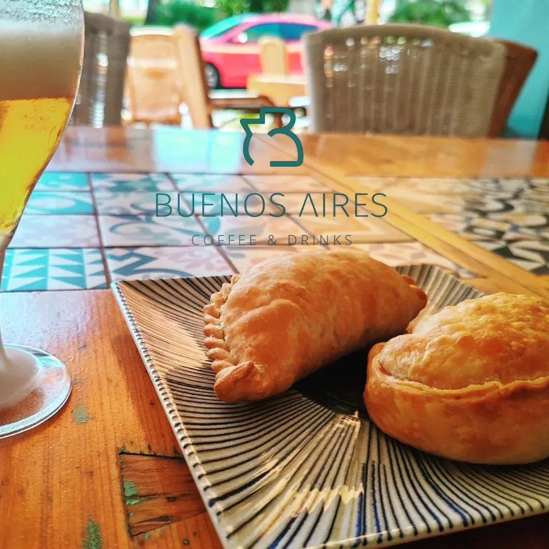 Empanadas en plato estampado con vaso de cerveza, sobre mesa de madera, ambiente de cafetería de Buenos Aires.
