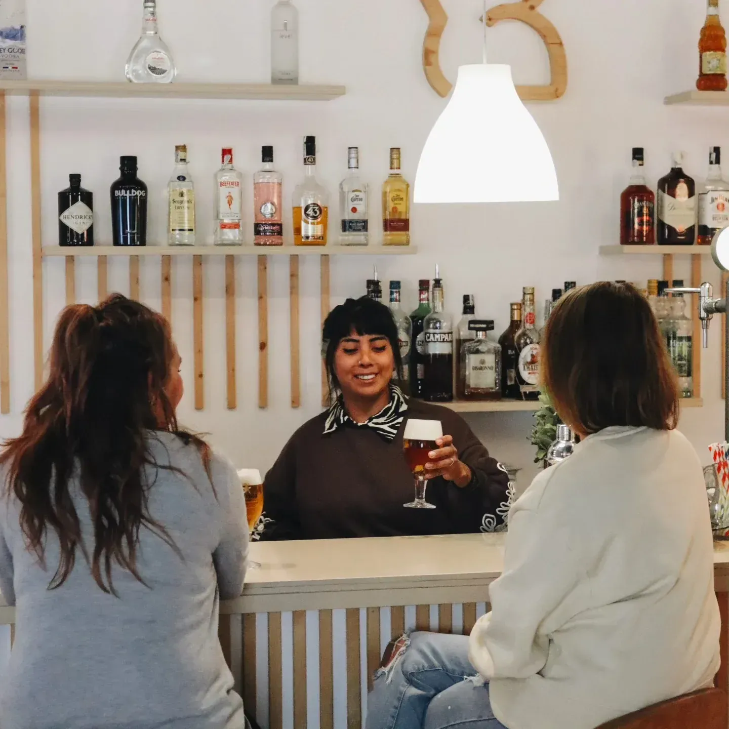 Un camarero sirve una cerveza a un cliente en un bar. Dos clientes están sentados frente al mostrador.