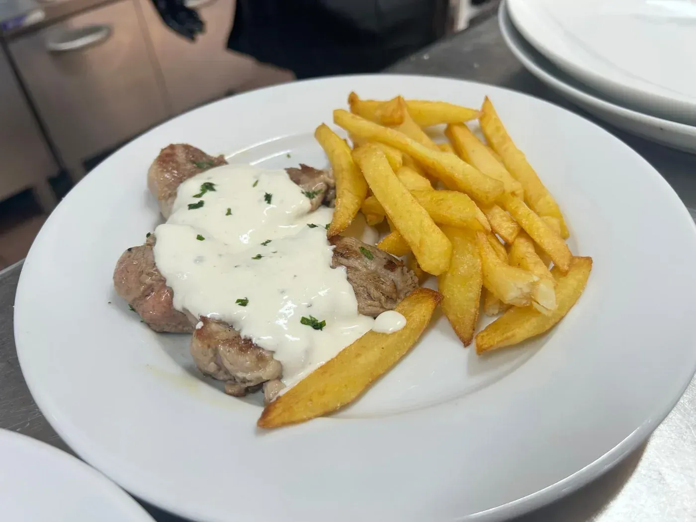 Interior de restaurante con mesas y sillas de madera, paredes de piedra y suelo de baldosas.