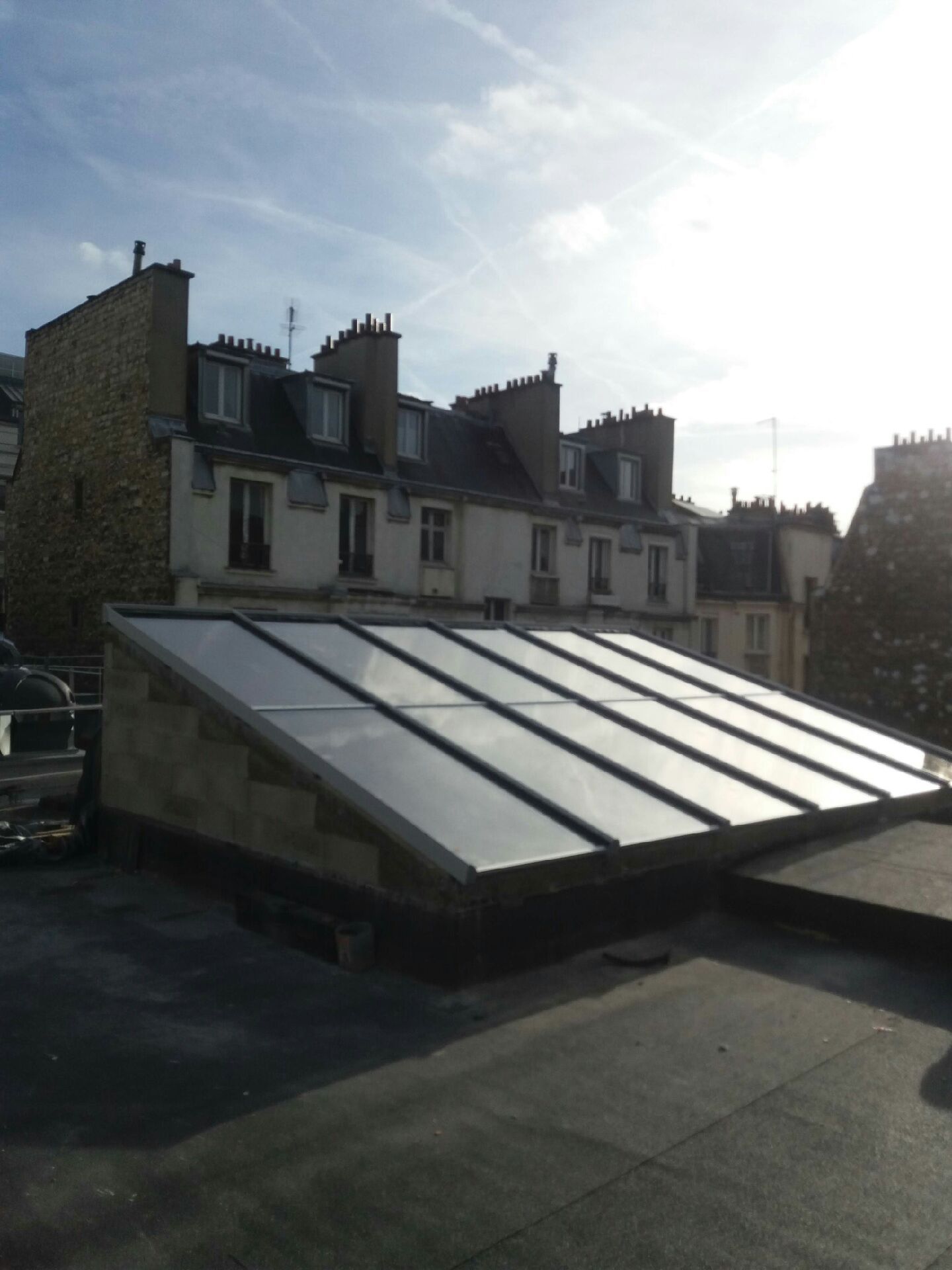 Une rangée de puits de lumière en verre installés sur un toit plat urbain, avec des immeubles d'habitation en arrière-plan.