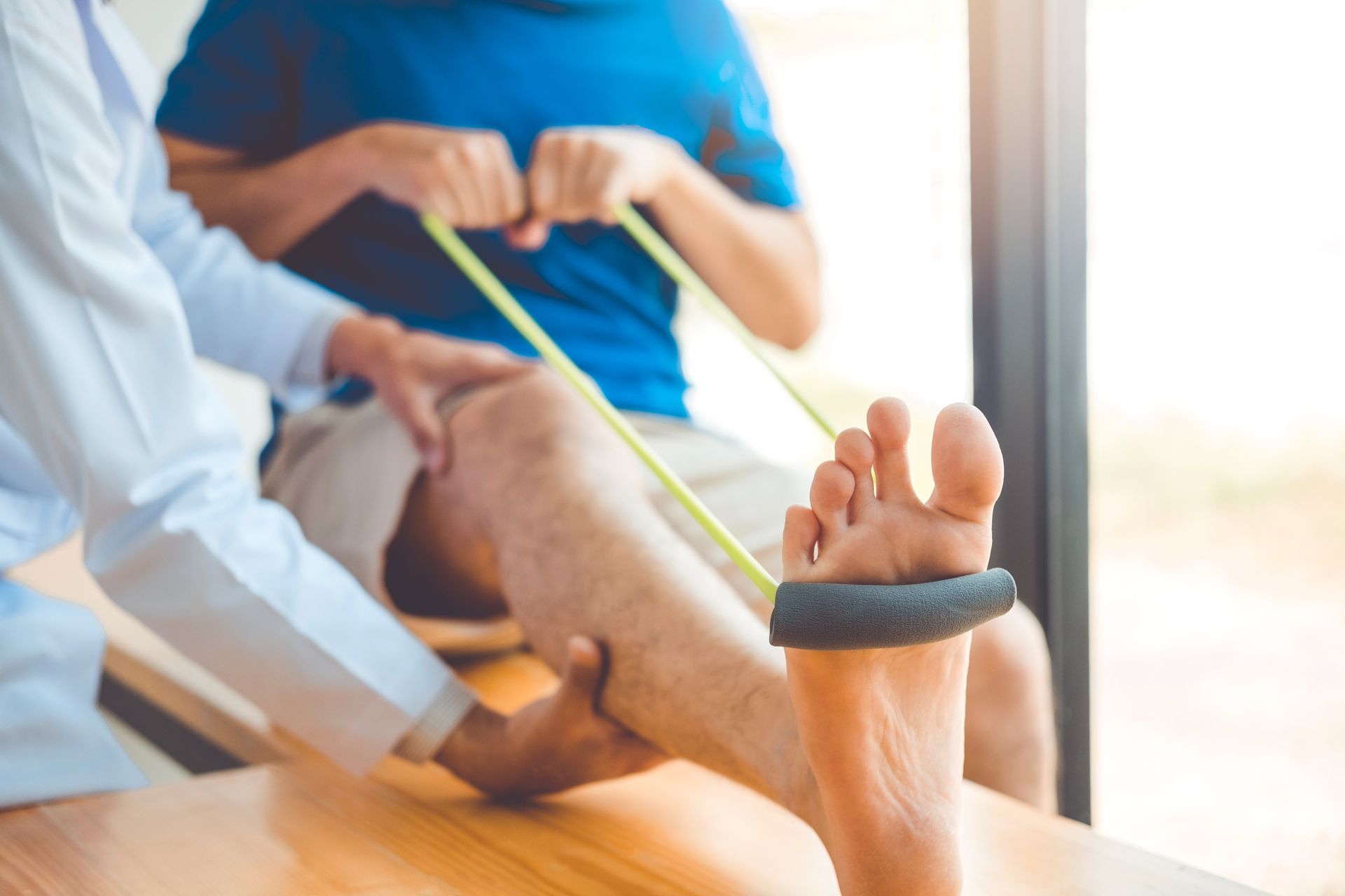 In einem hellen Studio hilft ein Physiotherapeut einem Patienten bei der Durchführung einer Beinübung mit einem gelben Widerstandsband.