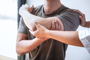 Ein Physiotherapeut untersucht die Schulter eines Patienten in einer hellen, geschlossenen Klinikumgebung.