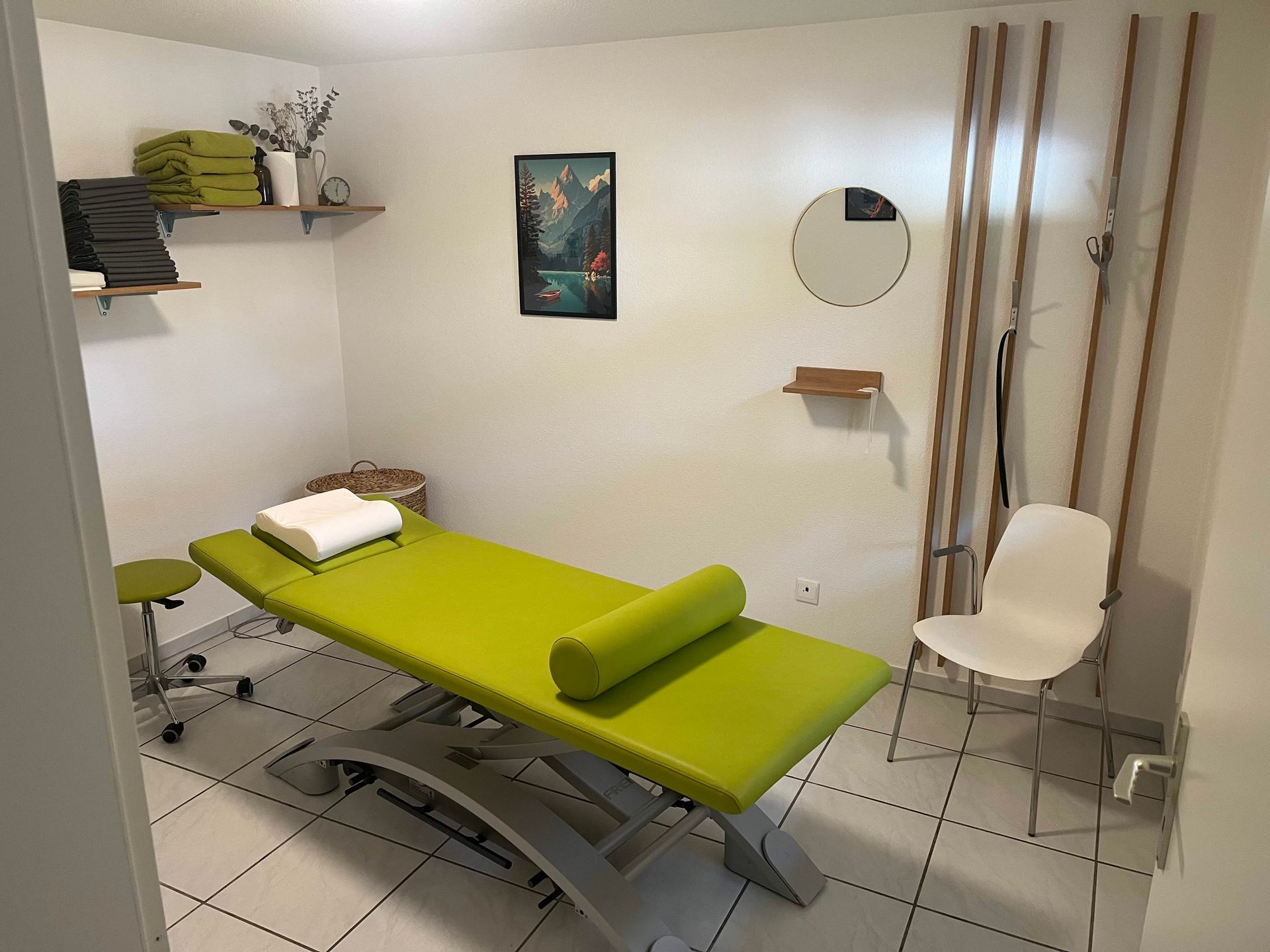 Ein Therapeut in einem blauen Hemd führt an einer Person, die in einem Behandlungsraum auf einer Massageliege liegt, eine Beindehnung durch.