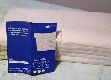 Ein Nackenstützkissen der Marke Adatte liegt auf einem Bett neben der dazugehörigen blauen Produktbroschüre.