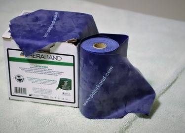Eine blaue TheraBand-Trainingswiderstandsbandrolle liegt neben ihrer Produktverpackung auf einer weissen Fläche.