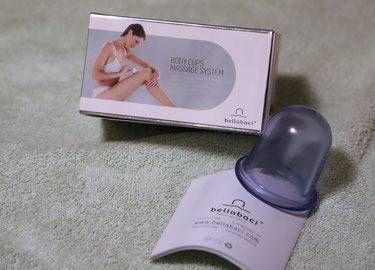 Ein BelleBaci Massage-Schröpfset, bestehend aus einer Box und einem abnehmbaren lila Silikon-Saugfuss auf einem weichen Stoff.