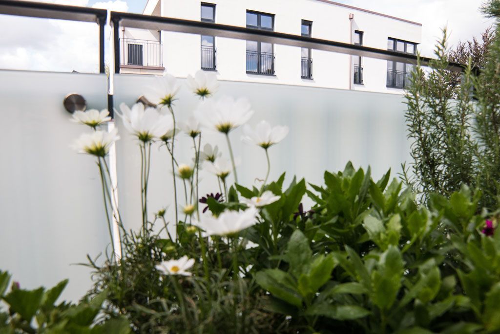Ein Zaun mit Blumen davor und einem Gebäude im Hintergrund
