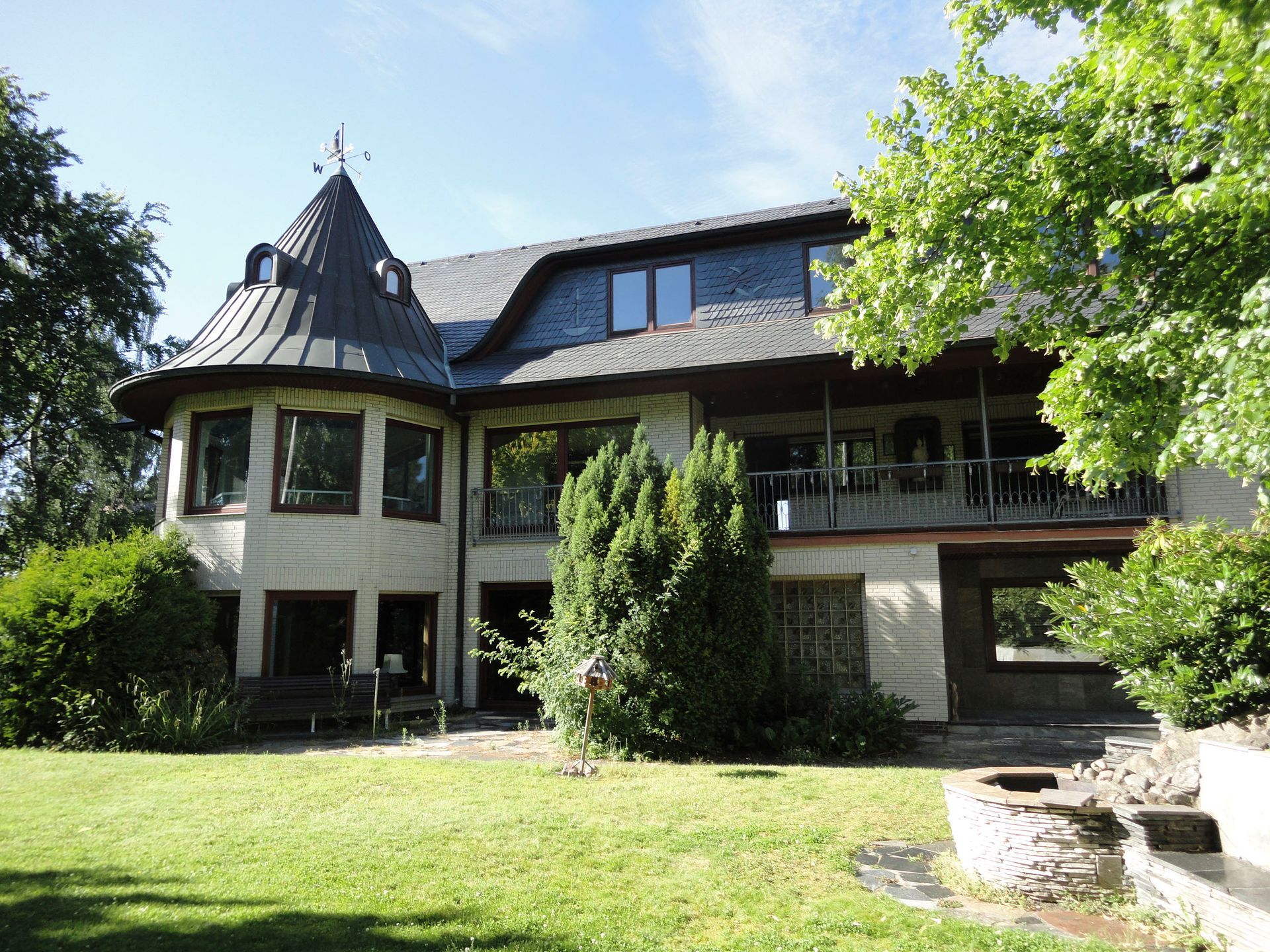 Ein großes Haus mit vielen Fenstern ist von Bäumen und Gras umgeben.