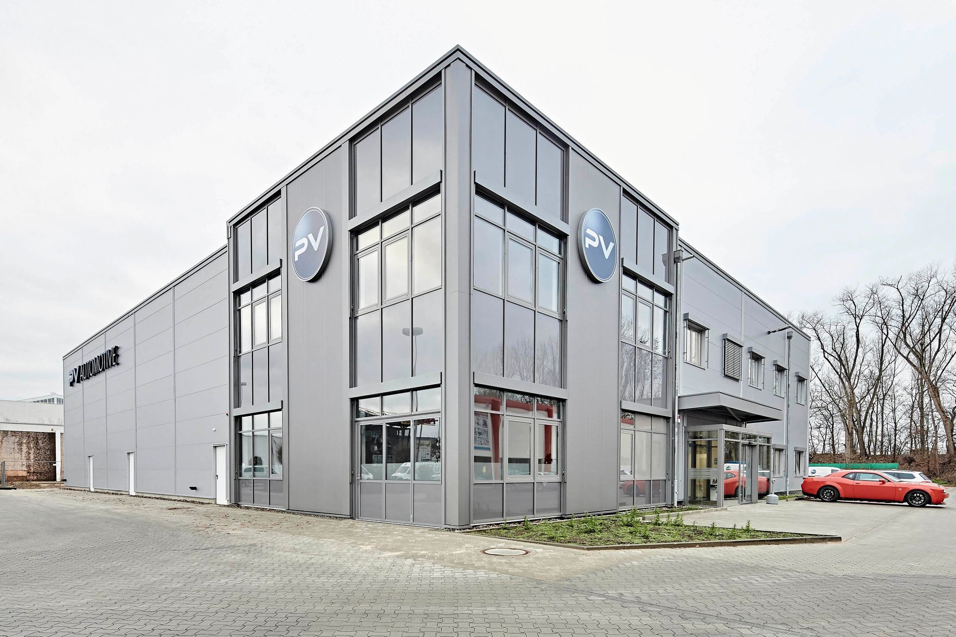 Ein großes graues Gebäude mit vielen Fenstern und einem davor geparkten roten Auto.