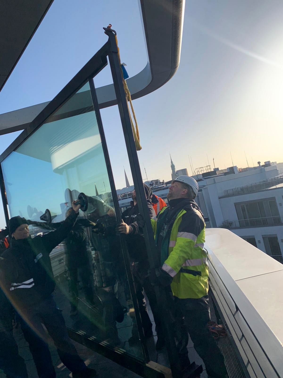 Eine Gruppe von Leuten steht auf dem Dach eines Gebäudes und hält ein großes Stück Glas.