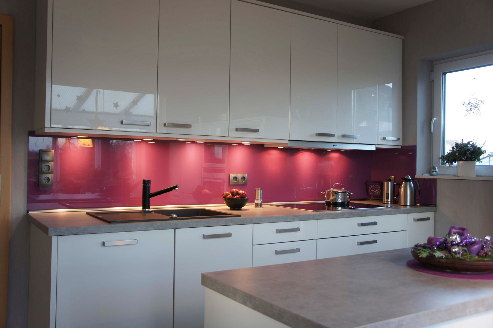 Eine Küche mit weißen Schränken und einer rosa Küchenrückwand