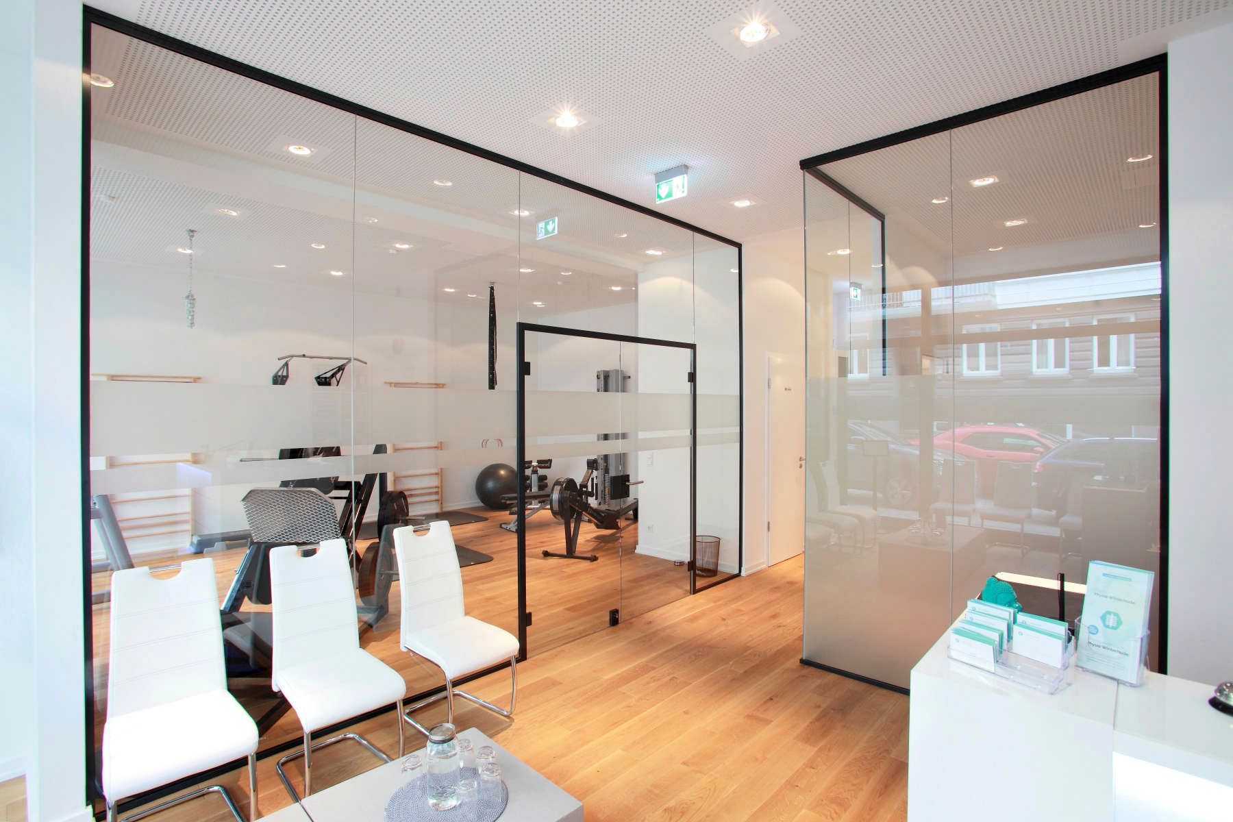 Ein Wartezimmer mit weißen Stühlen und einer Glaswand.