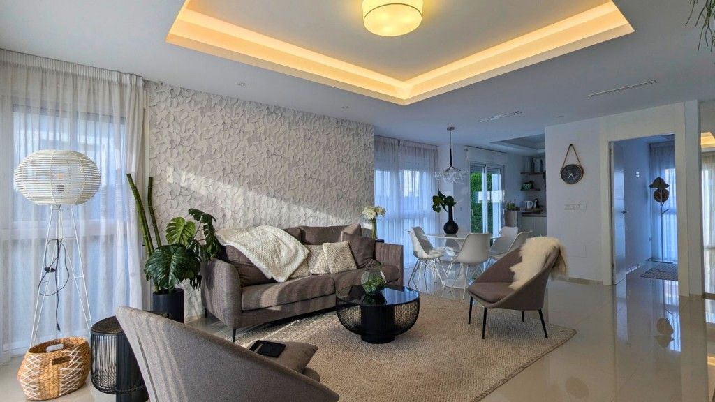 Sala de estar con sofá gris, pared texturizada y cortinas blancas.