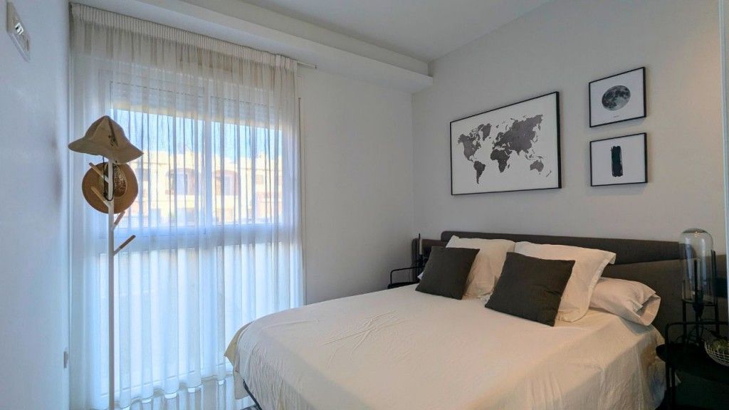 Dormitorio con cama doble, paredes blancas, ventana con cortinas transparentes, arte de mapa del mundo y perchero.