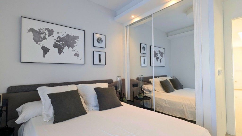 Dormitorio con decoración en gris y blanco, cama grande, arte de mapas del mundo y puertas de armario con espejos.