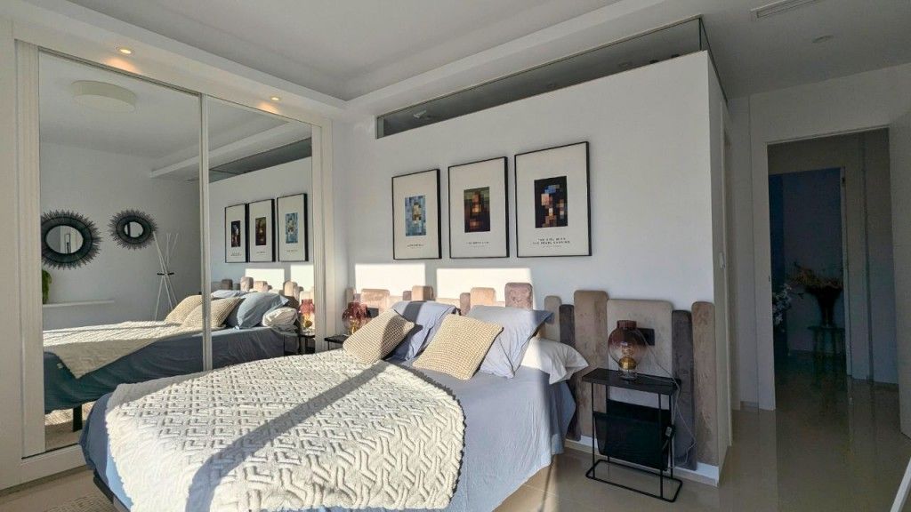 Dormitorio con cama, armario con espejo, arte enmarcado y una mesa pequeña.