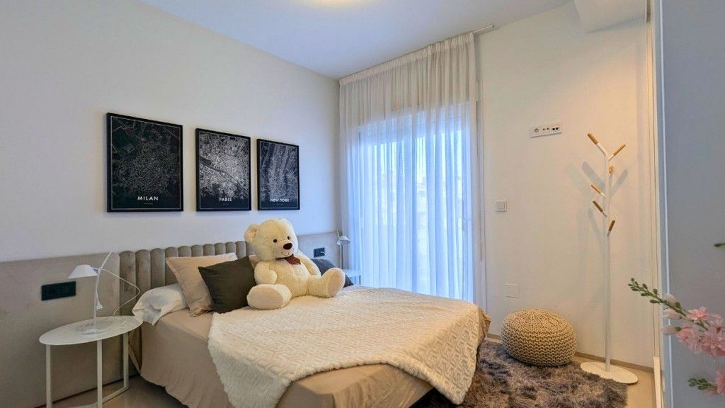 Dormitorio con cama, osito de peluche, obra de arte y ventana con cortinas.