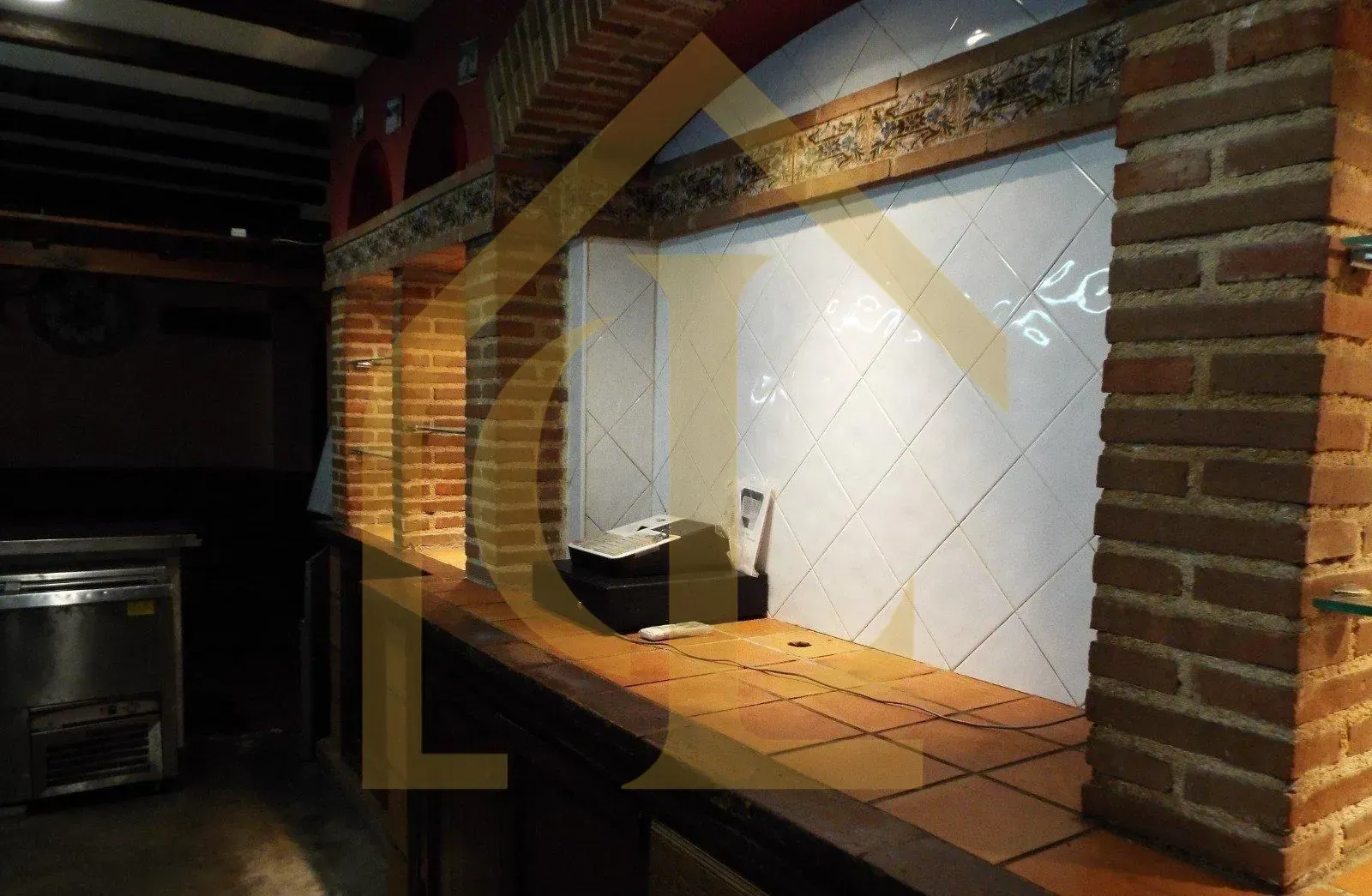 Abertura con marco de ladrillo y mostrador de madera; interior de azulejos blancos. Frigorífico visible a la izquierda.