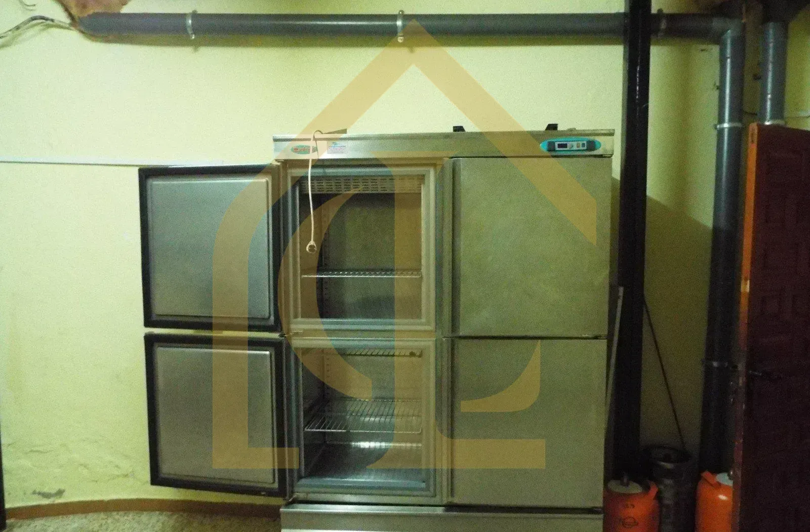 Un gran frigorífico de acero inoxidable con las puertas abiertas, en una habitación con tuberías.