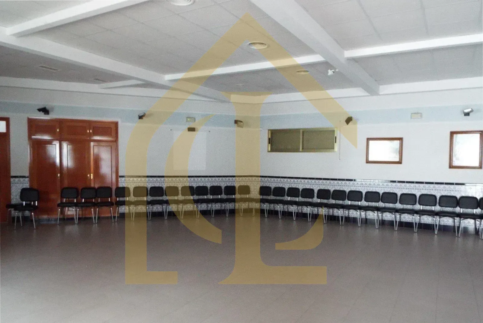 Habitación vacía con sillas dispuestas en círculo, puertas a la izquierda, ventanas a la derecha, luces en el techo.