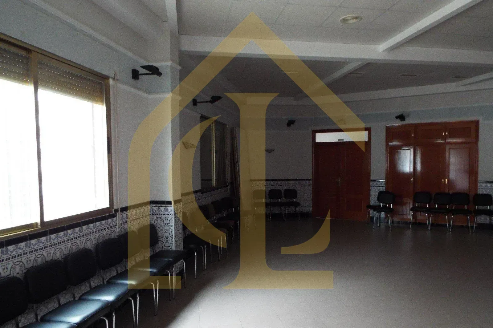 Habitación vacía con sillas contra una pared estampada, ventana a la izquierda, puertas a la derecha.