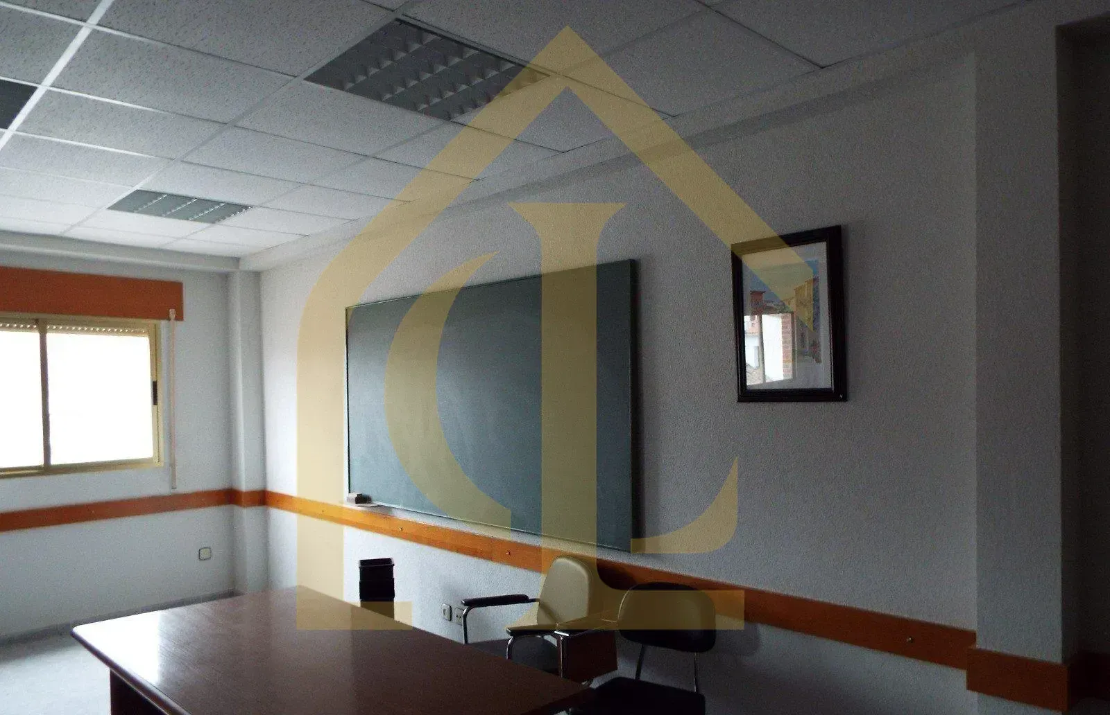 Sala de conferencias con pizarra, mesa, sillas y ventana con marco naranja.