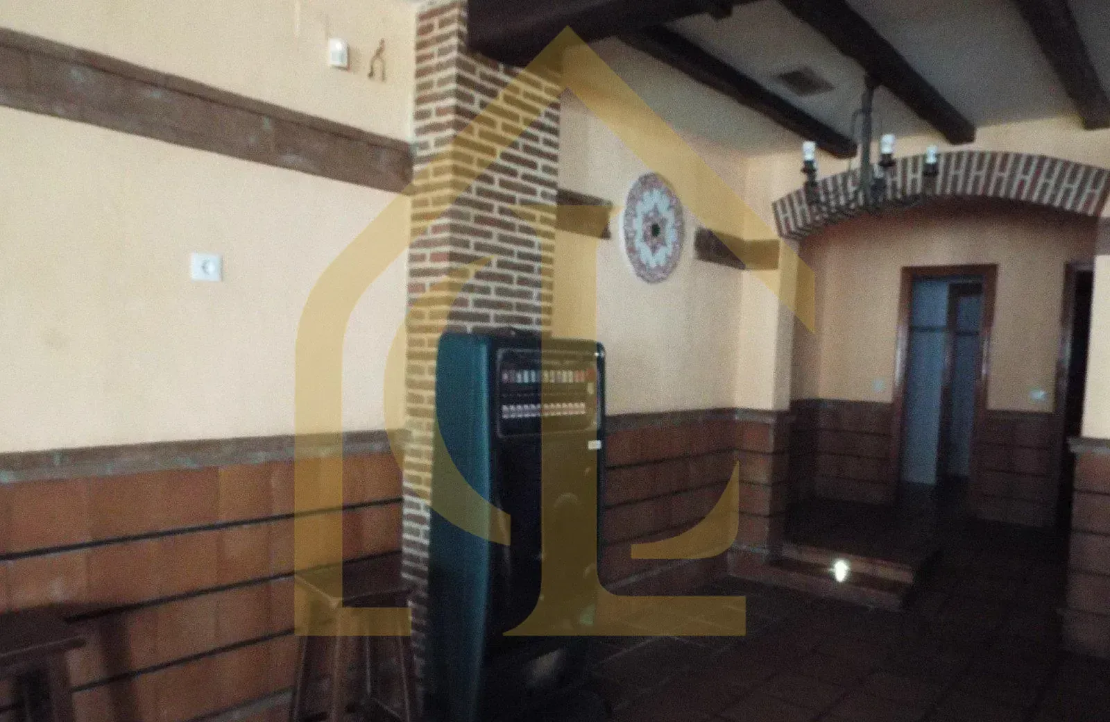 Interior de una habitación rústica con vigas de madera a la vista, columna de ladrillo y paredes alicatadas.