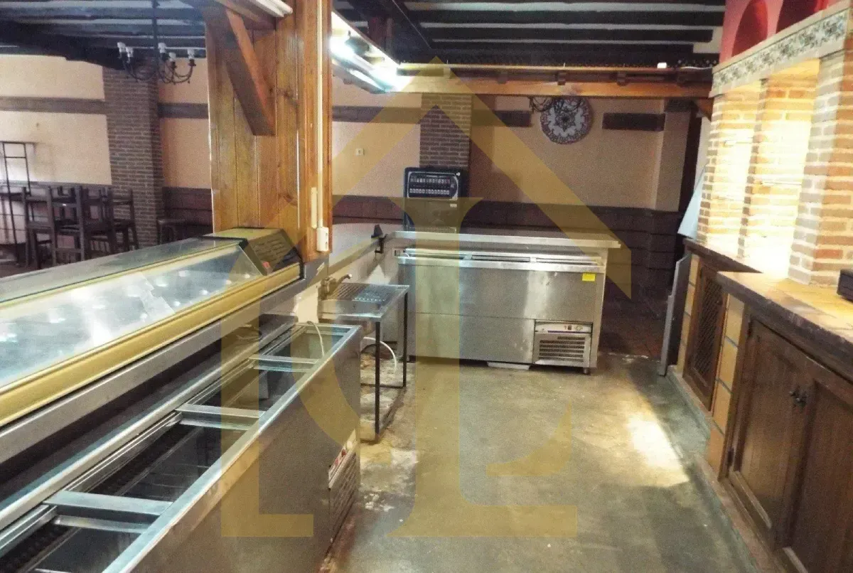 Interior de cocina comercial con encimeras y electrodomésticos de acero inoxidable. Pared de ladrillo y reloj a la vista.