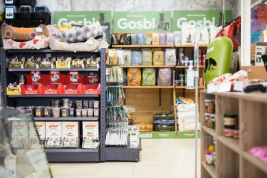 Interior de una tienda de mascotas con estantes llenos de comida, camas y otros suministros para mascotas.
