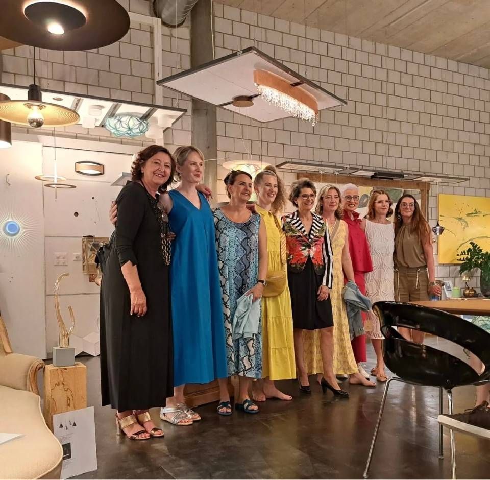 Eine Gruppe von Menschen posiert in farbenfrohen Outfits auf einer Bühne und lächelt in einem hellen Innenraum.