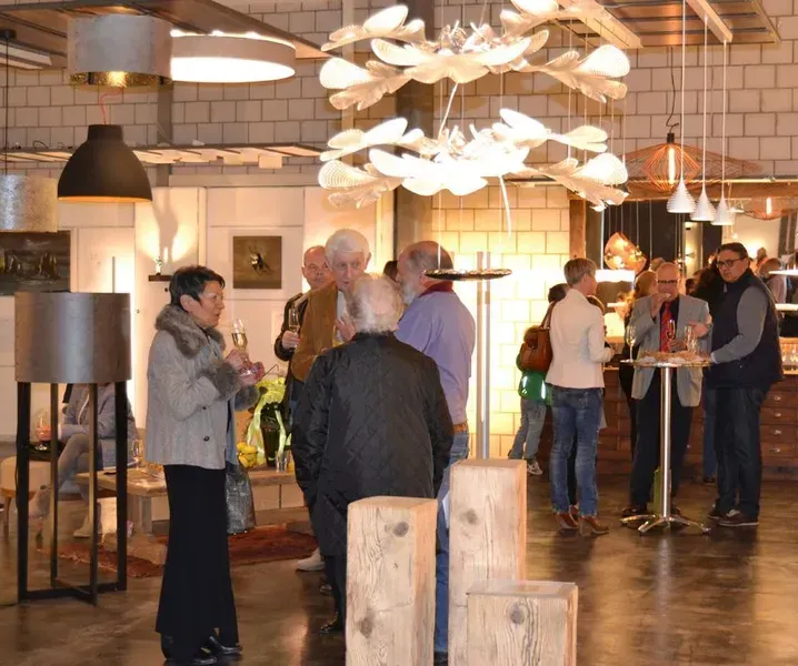 Menschen unterhalten sich in einem warm beleuchteten Café im Industriestil mit Pendelleuchten und Holztischen.