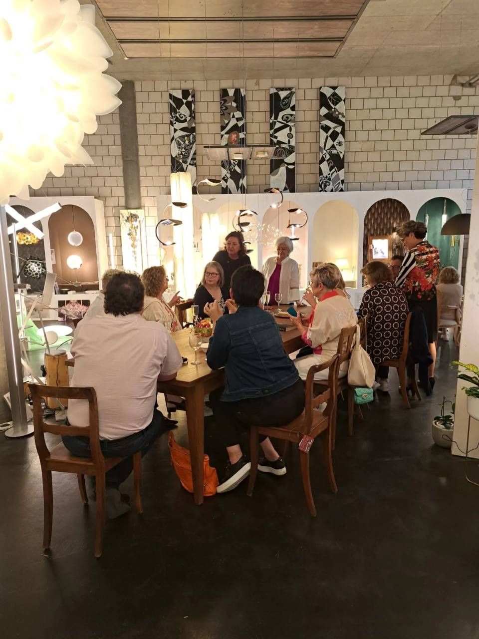 Menschen sitzen um Tische in einem hellen, modernen Restaurant oder Veranstaltungsraum mit Backsteinwänden und Hängelampen.