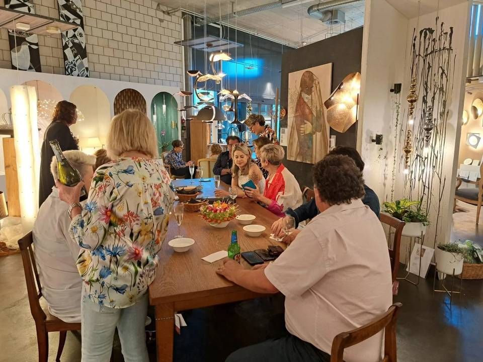 In einem hellen Café hatten sich die Menschen um einen langen Tisch versammelt und genossen bei einer lebhaften Zusammenkunft Getränke und Snacks.