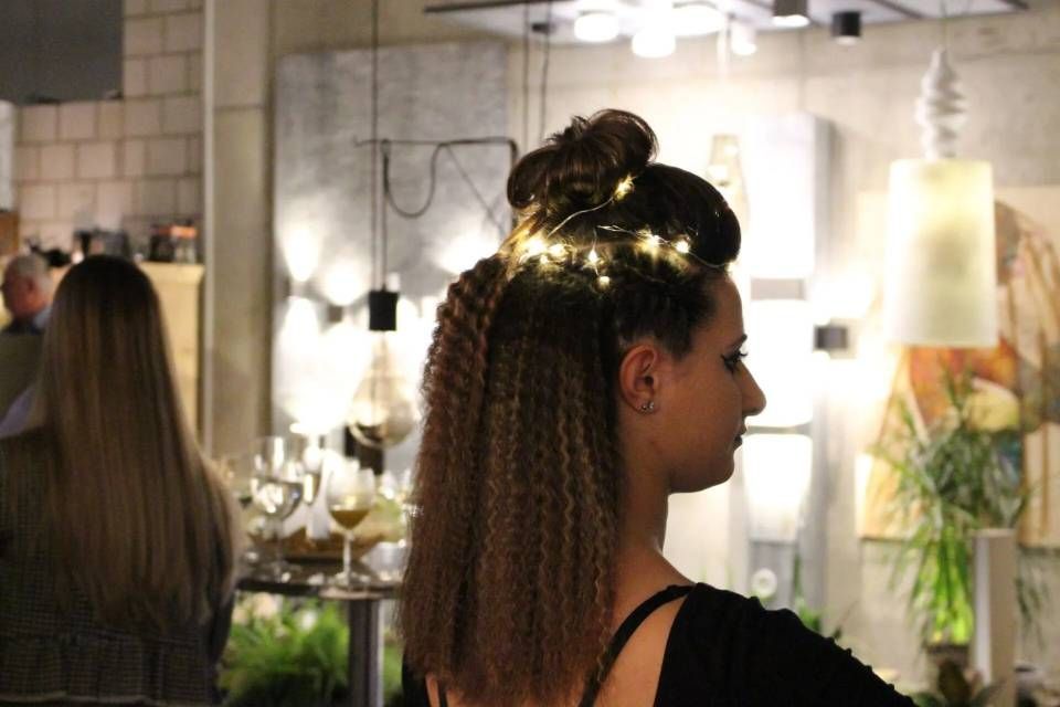 Frau mit geflochtenem Haar in einem hellen Salon, im Profil neben einem Spiegel und Blumen zu sehen.
