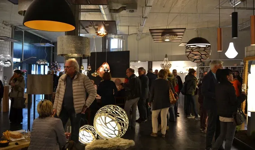 Menschen mischen sich in einer warm beleuchteten, modernen Galerie oder einem Ausstellungsraum mit hängenden Pendelleuchten.
