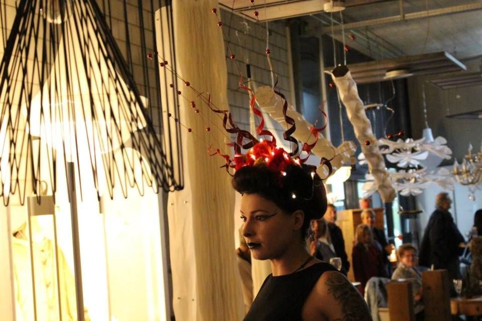 Frau mit rotem, gehörntem Kopfschmuck steht in einem warm beleuchteten Ausstellungsbereich einer Galerie.