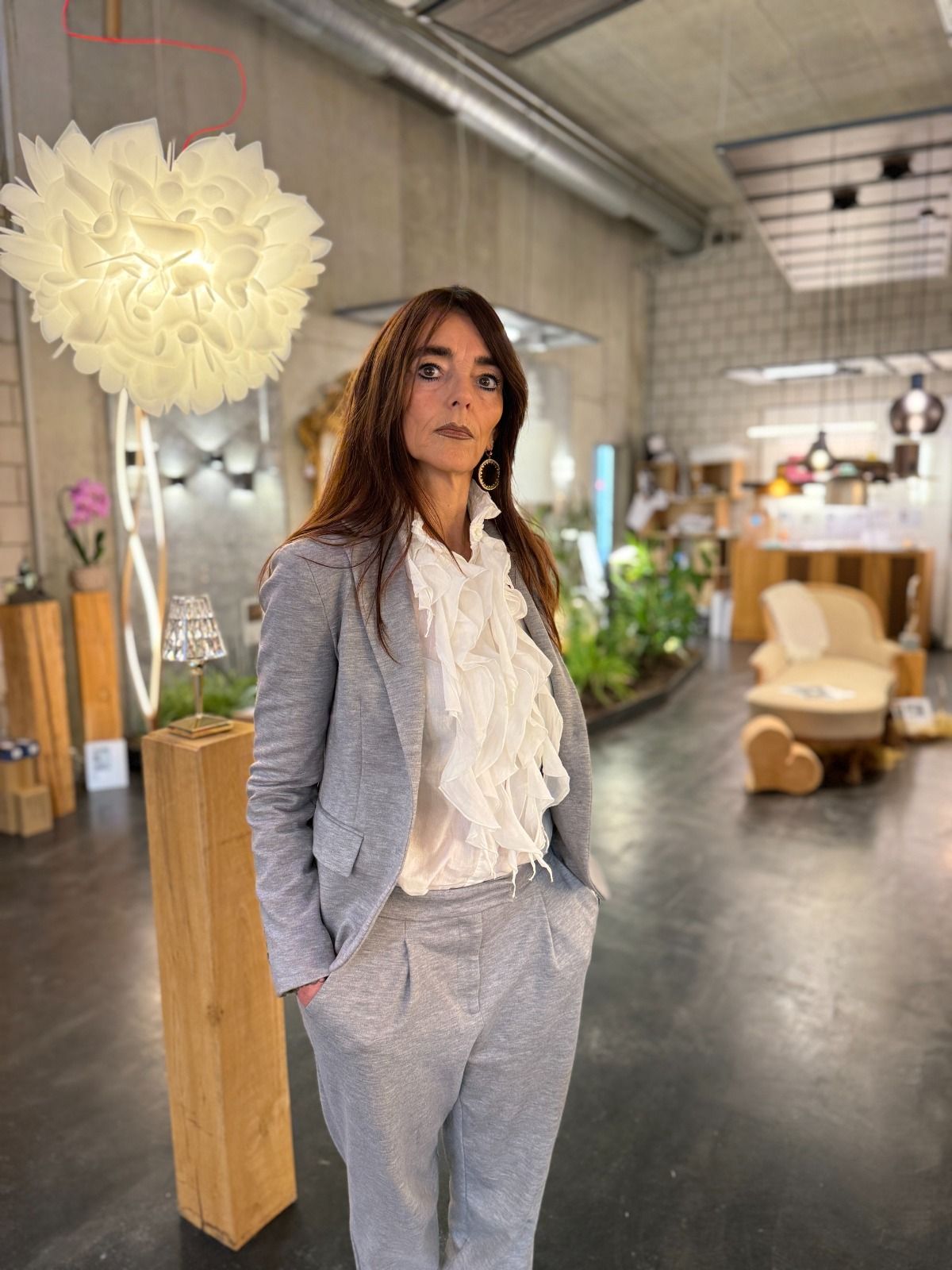 Porträt einer Frau mit langen dunklen Haaren und schwarzer Brille, die einen marineblauen Blazer trägt, vor beigem Hintergrund