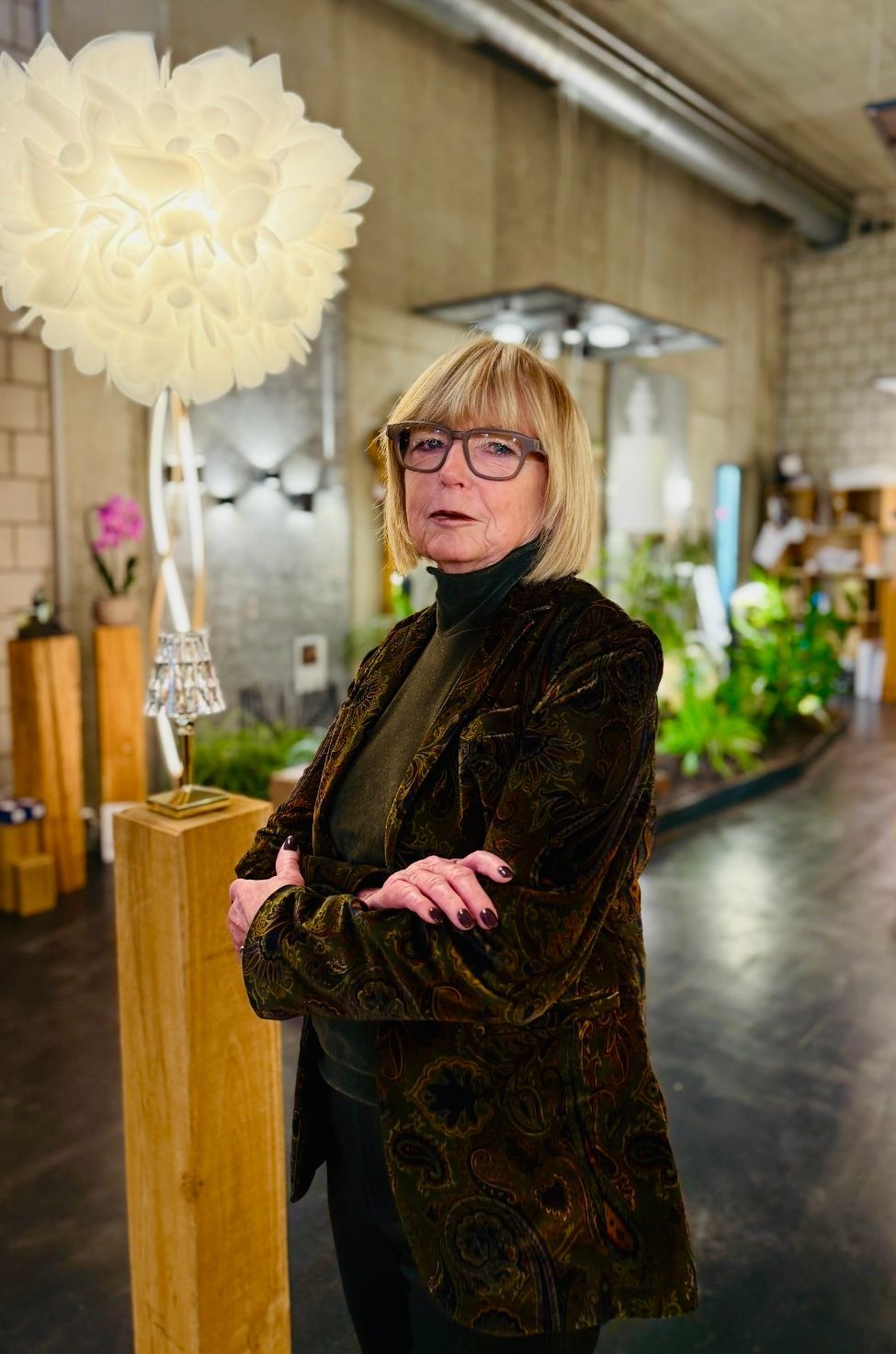 Frau in einem hellen Blazer lächelt mit verschränkten Armen bei einer Veranstaltung in geschlossenen Räumen