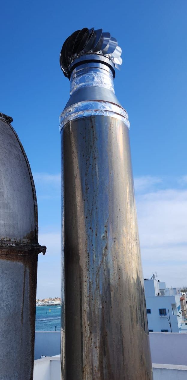 Una chimenea de acero inoxidable en la parte superior de un edificio con un cielo azul de fondo.