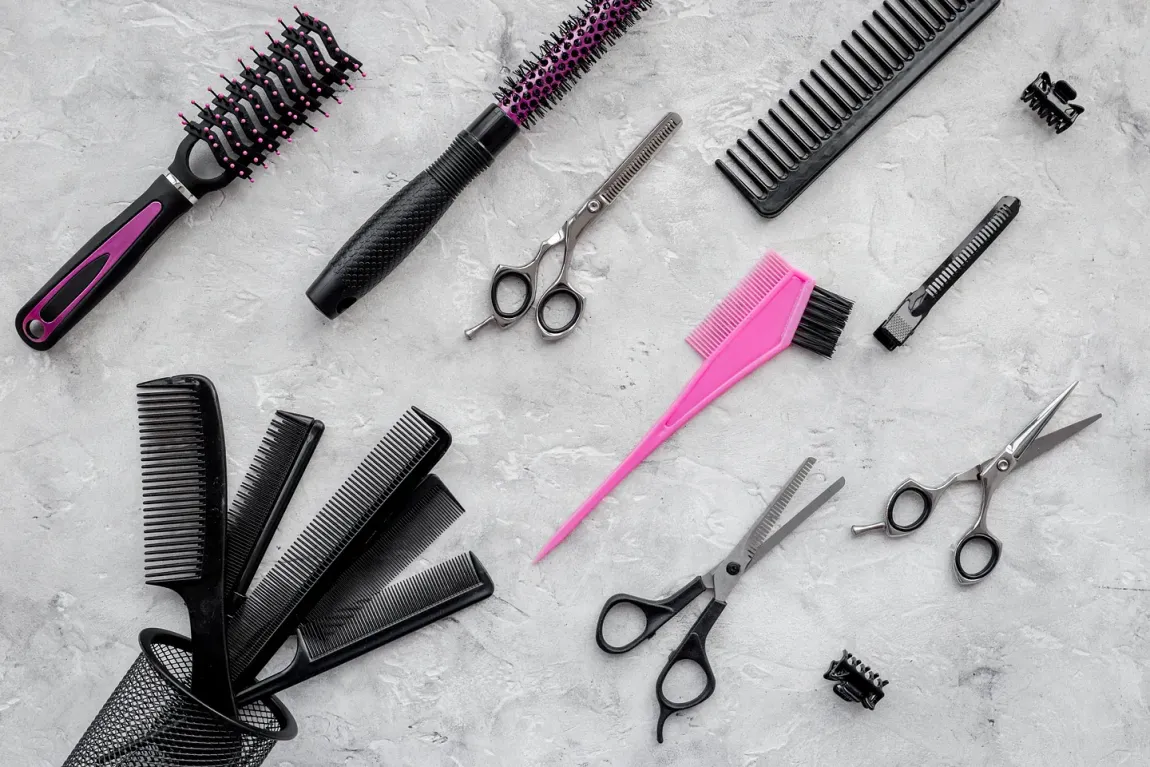 Un montón de cepillos para el cabello, tijeras y peines sobre una mesa.