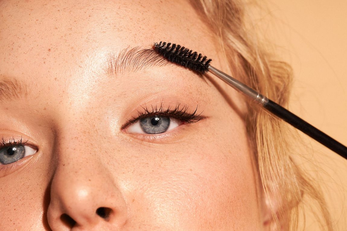 Gros plan d’une brosse de mascara appliquant du mascara noir sur les cils d’une personne blonde.