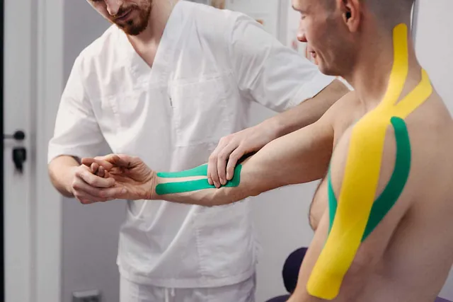 A un hombre le están colocando cinta kinesiológica en el brazo.
