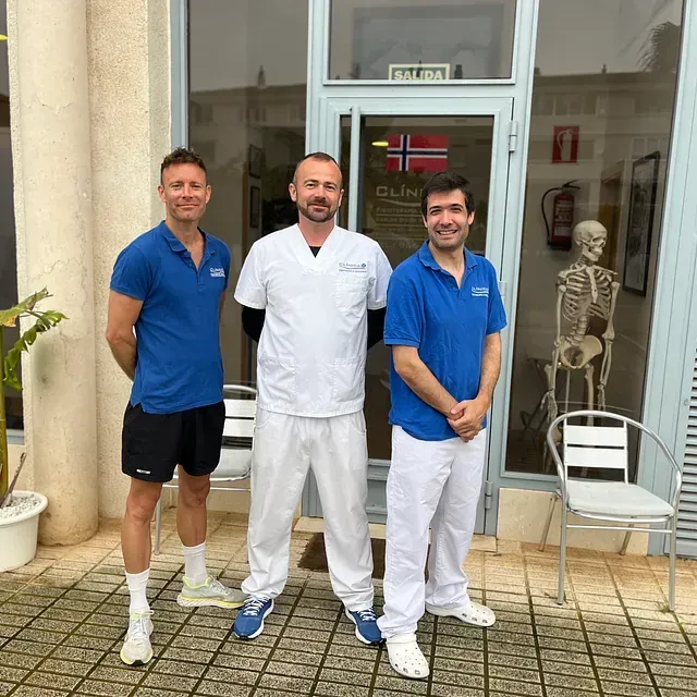 Tres hombres de pie frente a un edificio con un esqueleto al fondo.