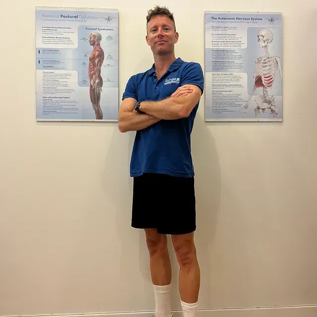 Un hombre con una camisa azul está de pie con los brazos cruzados.