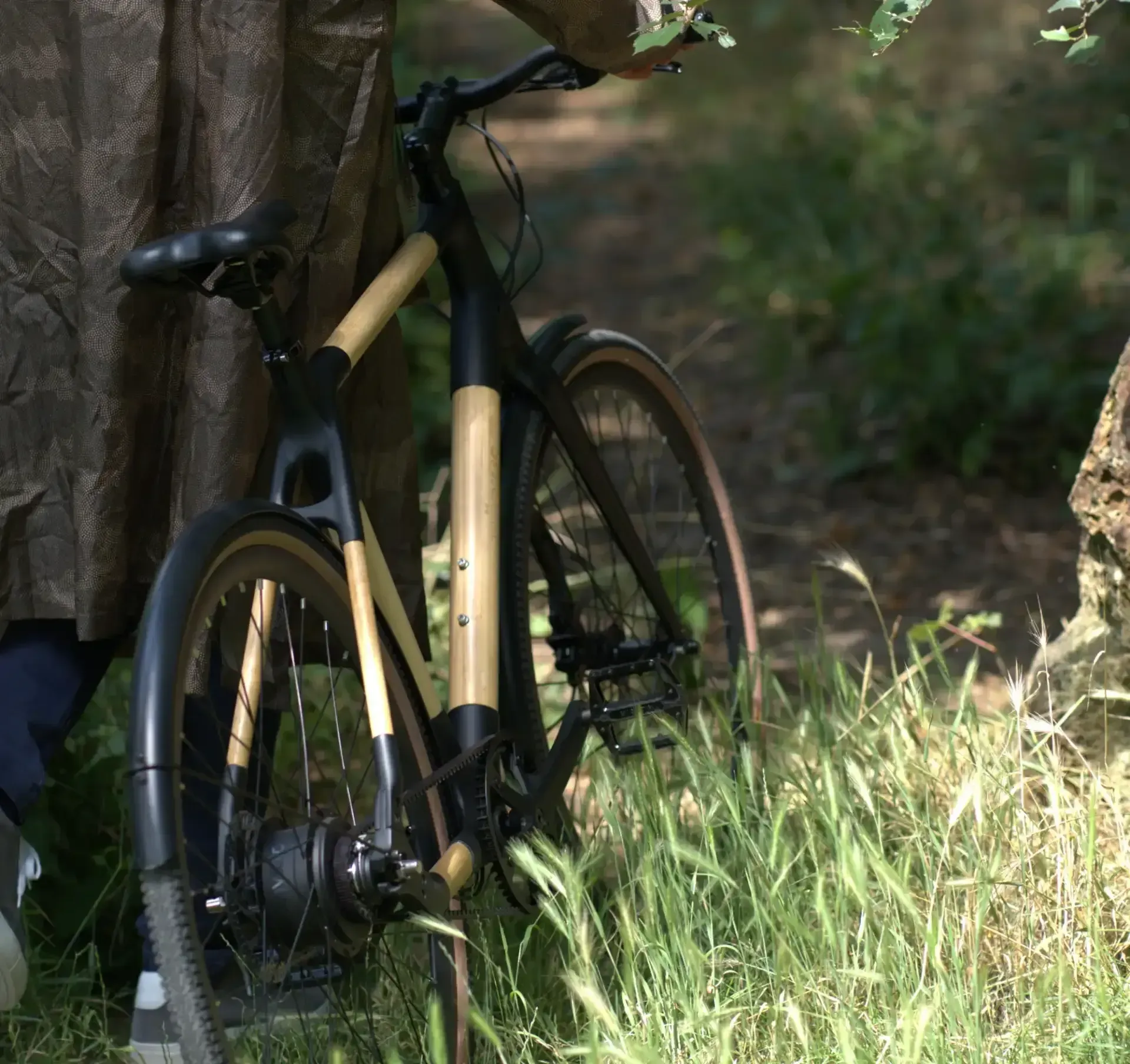 Un vélo en bambou est appuyé contre un arbre dans une zone herbeuse, mettant en valeur son cadre naturel.
